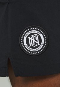 Shorts noirs avec un patch rond brodé portant le texte « Nike Football Club », entouré d'étoiles et d'une bordure décorative.
