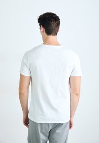 T-shirt blanc à manches courtes en coton, avec un col rond simple et une coupe décontractée. Vue de dos.