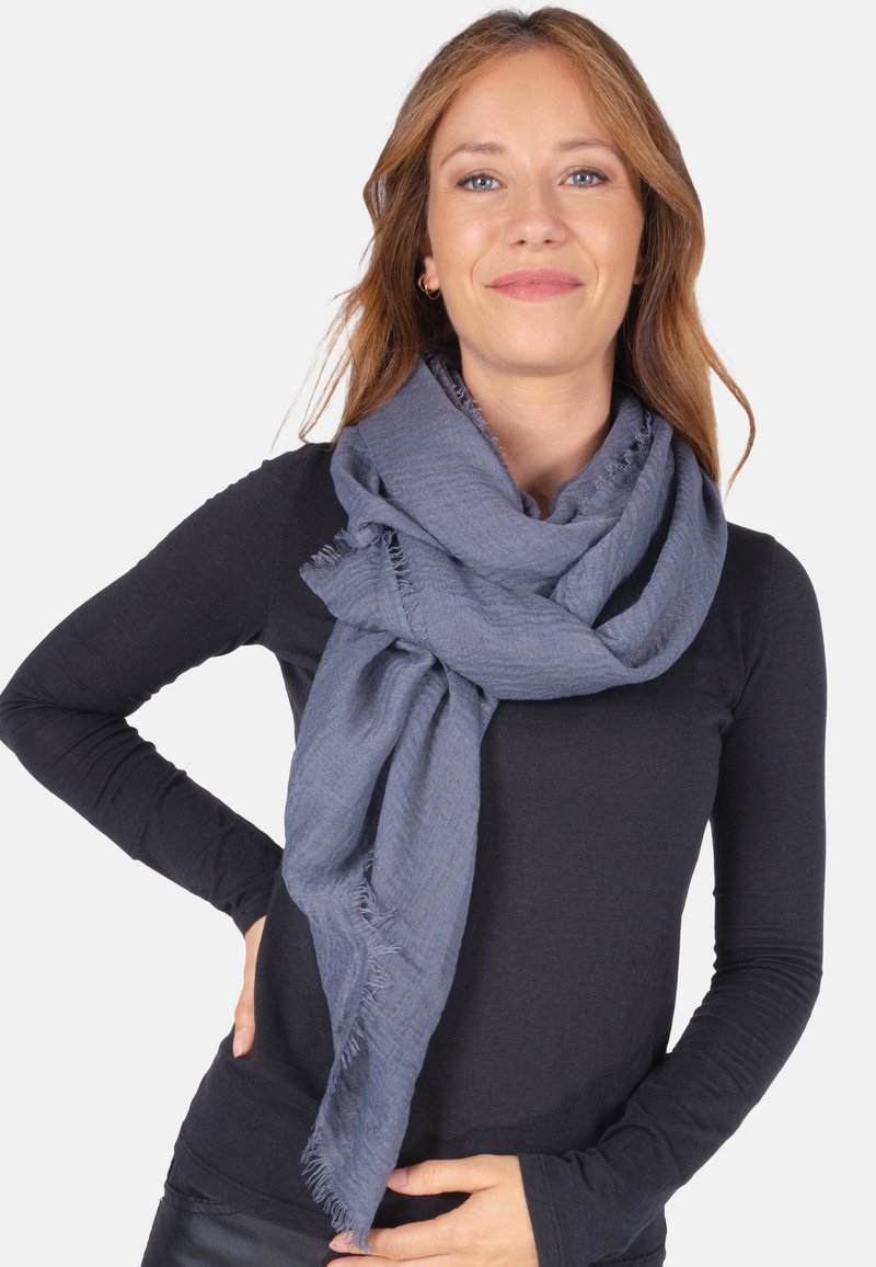Écharpe grise en tissu tissé avec des bords effilochés, drapée de manière décontractée autour du cou. Tissu léger, texture douce et design polyvalent.