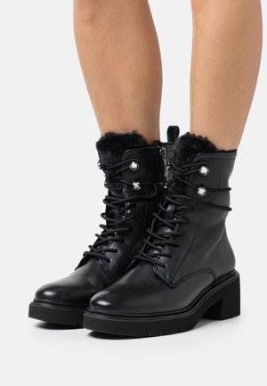 Bottes noires en cuir à la cheville avec un revers en fausse fourrure texturée, avant lacé, fermeture éclair latérale et talon épais. Présente des accents métalliques sur le revers.