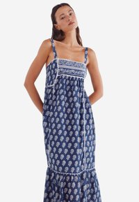 Robe maxi en tissu bleu marine avec des motifs de feuilles blanches, dotée d'un décolleté carré, de bretelles spaghetti et d'une jupe froncée.