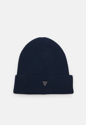 Bonnet en tricot côtelé bleu foncé avec bord plié, présentant un petit logo métallique triangulaire sur un fond uni.
