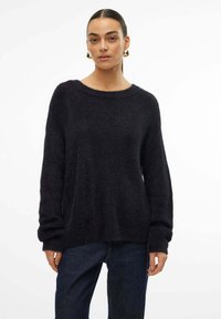 Zwarte gebreide trui met een brede halslijn, lange mouwen en een losse pasvorm. Draagt over donkere jeans, met subtiele gebreide details door het geheel.