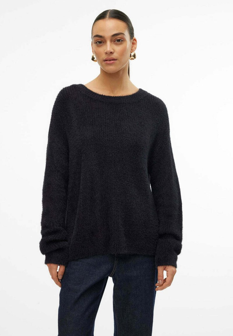 Zwarte gebreide trui met een brede halslijn, lange mouwen en een losse pasvorm. Draagt over donkere jeans, met subtiele gebreide details door het geheel.