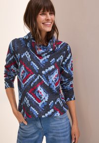 Maglione con collo a lupetto in grigio scuro con un motivo geometrico blu, rosso e bianco. Maniche lunghe e vestibilità rilassata con tessuto testurizzato.