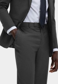 Grå skræddersyet jakkesæt med en tekstureret stof, der har en tætsiddende silhuet, båret med en hvid skjorte og et marineblåt prikket slips.