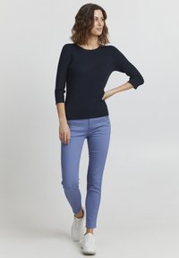 Granatowy sweter o prążkowanej strukturze z rękawami do łokcia, w zestawieniu z jasnoniebieskimi jeansami o wąskim kroju z bocznymi wypustkami i srebrnymi guzikami.