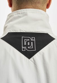 White jacket collar with black diamond patch featuring white embroidered logo. Smooth texture, modern design. Back view focus.