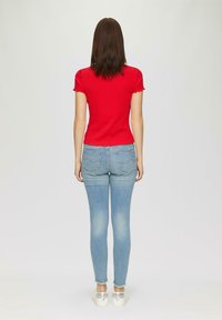 Rode kortemouwen bovenstuk gecombineerd met lichtblauwe skinny jeans. De outfit heeft een getailleerd ontwerp met golvende mouwen en subtiele achterzakken.