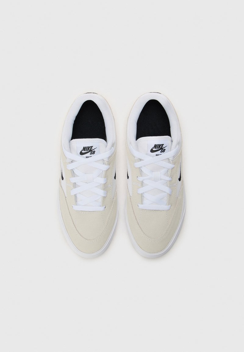 Zapatillas Nike SB en suave ante beige claro, con forro interior de tela negra, cordones blancos y detalles del logo. Punta redondeada y suela de goma plana.