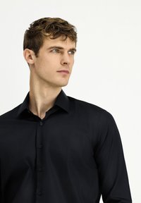 Zwart langærmelig shirt met een slanke pasvorm, een knoopsluiting aan de voorkant en een gladde textuur. Heeft een klassieke kraag en subtiele knoopdetails.