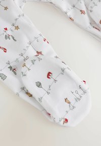 Tissu blanc douillet avec des motifs festifs, comprenant des bonshommes en pain d'épice, des cannes en sucre, des cloches de Noël et des branches de houx. Détail de poignet doux visible.