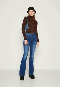 Rudas raštuotas megztinis su aukšta apykakle, mėlyni plačios kojos džinsai, juodi platforminiai batai ir maža mėlyna rankinė. Modelis stovi prieš šviesią fono.