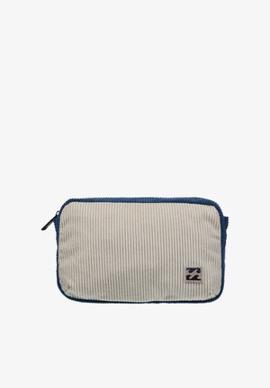 Pochette en velours côtelé avec une texture côtelée couleur crème, des bords bleus et une fermeture éclair noire. Comprend un écusson logo sur le devant.