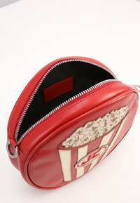 Röd läder crossbody-väska formad som en popcornbehållare, med ett blixtlås, tygfoder och en detaljrik popcorn-grafik på framsidan.