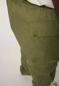 Close-up van olijfgroene cargobroek met grote zijzak en elastische tailleband, gedragen met een lichtbeige top.