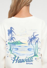 Kremowy sweatshirt z kolorową grafiką przedstawiającą palmy, góry i fale oceanu. Tekst brzmi "Hawaje" oraz "Ripcurl" w stylizowanej czcionce.