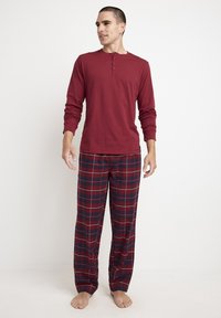 Red long-sleeve henley shirt with button placket paired with plaid pajama pants in dark red, navy, and white. Soft, relaxed fit.