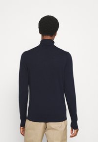Marineblaue Rollkragenpullover aus weichem Strickstoff, mit langen Ärmeln und gerippten Bündchen und Saum für eine enge Passform. Rückansicht dargestellt.