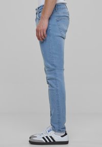 Világoskék, slim fit farmernadrág, öt zsebes kialakítással, enyhe koptatásokkal, fehér és fekete sportcipőkkel viselve.
