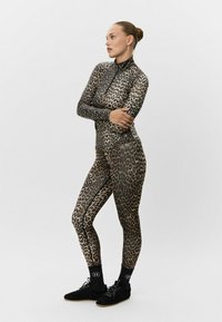 Bodysuit de leopardo de cuerpo entero con mangas largas y cuello alto. Fabricado con material flexible, presenta detalles en negro y zapatos deportivos.
