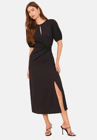 Musta midimekko teksturoidulla kankaalla, lyhyet pussihihat, vyötäröllä kiertoelementti ja vasemmalla puolella reikä reisikorkeudella.