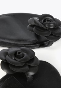 Zapatos de cuero negro tipo mocasín con dos acentos florales hechos del mismo material. Textura suave con un diseño redondeado.