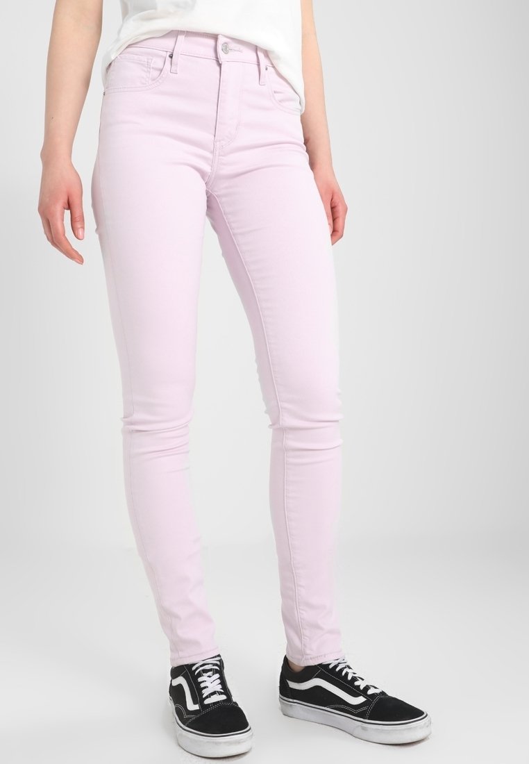 Mannequin portant un jean skinny rose clair associé à des baskets noires et blanches sur un fond gris uni.
