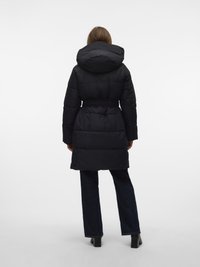 Fekete kapucnis puffadt kabát, öves kialakítással és térd alá érő hosszúsággal. Sima anyagú, steppelt paneles. Sötét farmer és csizma fölött viselve.