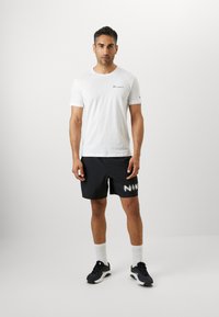 White cotton t-shirt with a small logo, paired with black shorts featuring a white "NIK" graphic. Worn with black sneakers and white socks.
