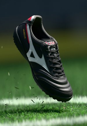 Fekete focicipő fehér kiegészítőkkel, texturált felülettel és kerek stoplival. Piros márkajelzés, fűzők és párnázott mandzsetta jellemzi.