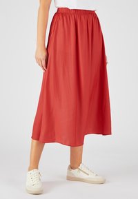 Falda midi roja con cinturilla elástica, hecha de tejido ligero y con un diseño fluido. Se lleva con zapatillas blancas.