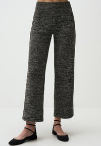 Weite, gestrickte Hosen mit einem schwarz-weißen Muster. Mit hoher Taille und geripptem Material. Kombiniert mit schwarzen flachen Schuhen.
