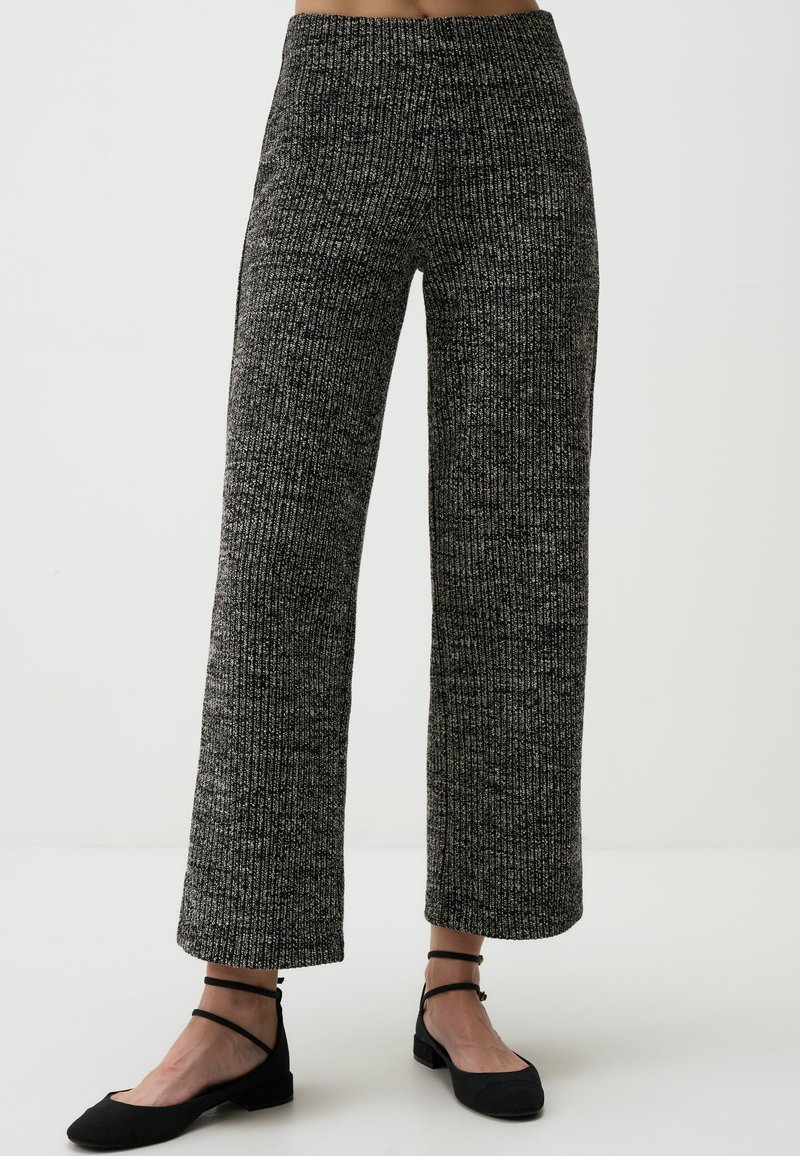 Weite, gestrickte Hosen mit einem schwarz-weißen Muster. Mit hoher Taille und geripptem Material. Kombiniert mit schwarzen flachen Schuhen.