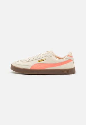 Beige leather sneakers with pink accents and gold logo. Features a textured brown rubber sole and white laces. Classic low-top design.