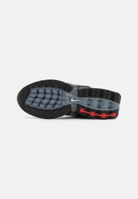 Suela de zapatilla de running Nike en negro y gris, con una superficie de goma texturizada, acentos rojos visibles y un diseño de banda de rodadura con patrón.