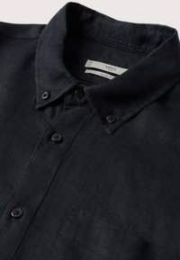 Camisa de lino negra con cuello botón, que presenta tres botones negros, un bolsillo en el pecho y un diseño ajustado.