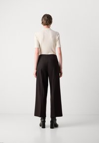 Crème kleurige ribbelstof top met korte mouwen, gecombineerd met hoge zwarte wijde broek. Zwarte enkellaarsjes maken de outfit af. Minimalistisch ontwerp.