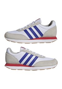 Białe buty sportowe z szarymi zamszowymi akcentami i trzema niebieskimi paskami po bokach. Charakteryzują się czerwonymi podeszwami i białymi sznurowadłami. Klasyczny design.