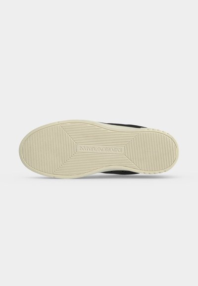 Semelle d'une chaussure noire avec une semelle en caoutchouc beige affichant une adhérence texturée et le logo Emporio Armani embossé au centre.