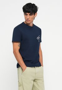Mørkeblå bomulds t-shirt med rund hals og korte ærmer; har et hvidt grafisk print på venstre bryst og en afslappet pasform.