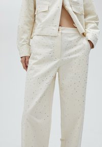 Crème kleurige broek met een gladde textuur, versierd met zilveren rhinestones in een verspreid patroon, met een ontspannen pasvorm.