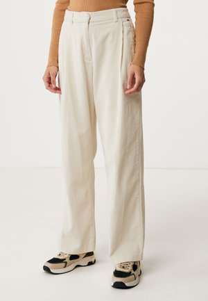 Pantaloni in corduroy color crema con una vestibilità ampia, caratterizzati da righe verticali e vita alta. Abbinati a sneaker sportive nere e beige.
