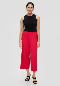 Rode geplooide culottes met een elastische tailleband, gecombineerd met een strakke zwarte mouwloze top. Gemaakt met zwarte blokhak sandalen.
