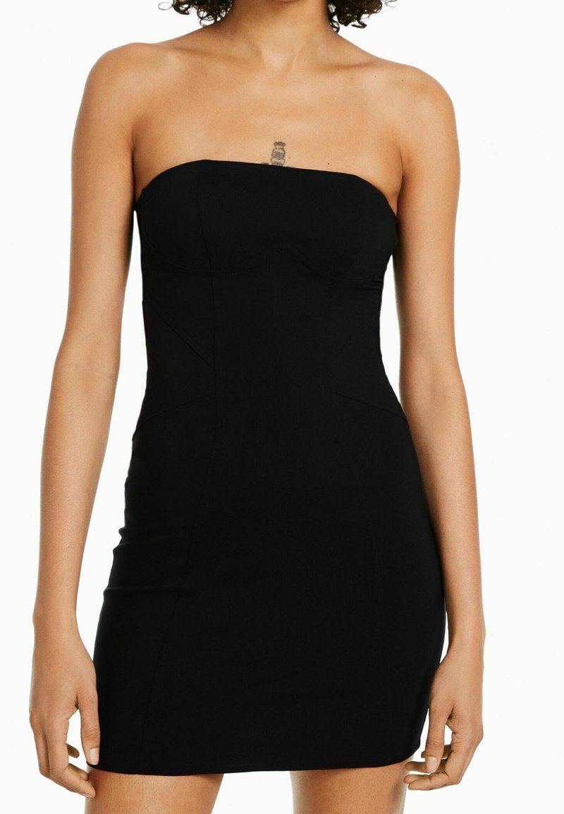 Černé šaty bez ramínek vyrobené z elastické látky. Mají přiléhavý střih, boční švy a délku do poloviny stehna. Hladký povrch, bez viditelných zapínání.