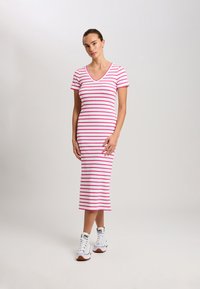 Gestreiftes Midikleid in Weiß und Pink, mit V-Ausschnitt und kurzen Ärmeln. Trägt dazu weiße High-Top-Sneaker.