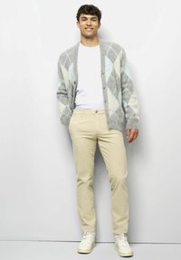 Grauer Cardigan mit blau-weißen Rautenmuster, getragen über einem weißen T-Shirt und kombiniert mit beigen Hosen und weißen Turnschuhen.