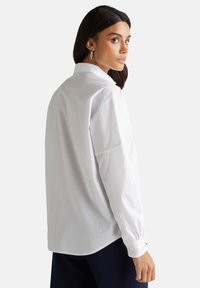 Camicia bianca a maniche lunghe con colletto, polsini con bottone e vestibilità comoda, realizzata in morbido tessuto di cotone.