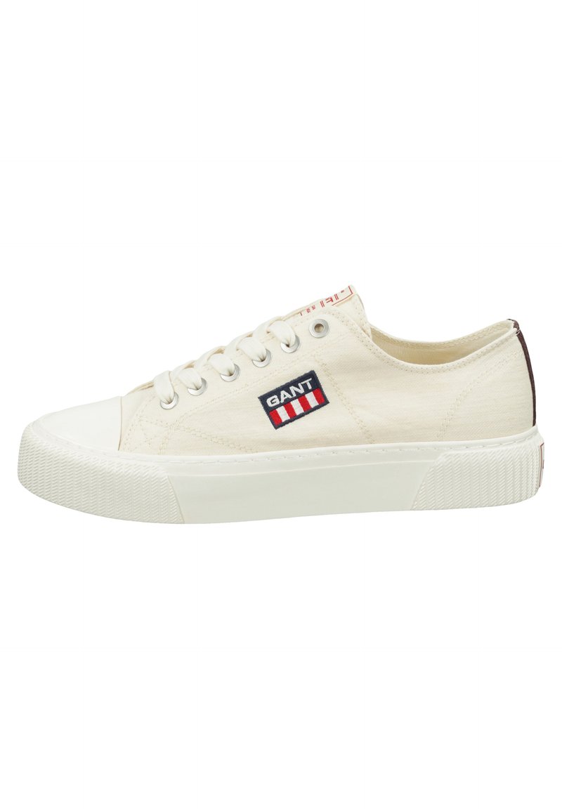 Zapatillas de tela en color crema con una puntera y suela de goma blanca. Presenta un parche con el logo de GANT con franjas rojas y azules. Diseño de corte bajo.