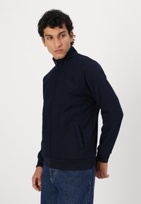 Laivan sininen vetoketjullinen takki, jossa on pystykaulus, kaksi sivutaskua ja ribattu hihansuu; valmistettu sileästä kankaasta, joka on slim fit -tyylinen.